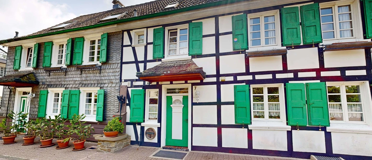 Ferienwohnung Haan Fachwerkhaus von außen, mit grünen Fensterläden und Blumen vor der Tür.