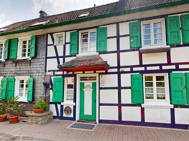 Ferienwohnung Haan Fachwerkhaus von außen, mit grünen Fensterläden und Blumen vor der Tür.