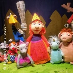 Bunte Handpuppen rund um eine kleine Hexenfigur stehen vor einer Kulisse mit Waldmotiv.