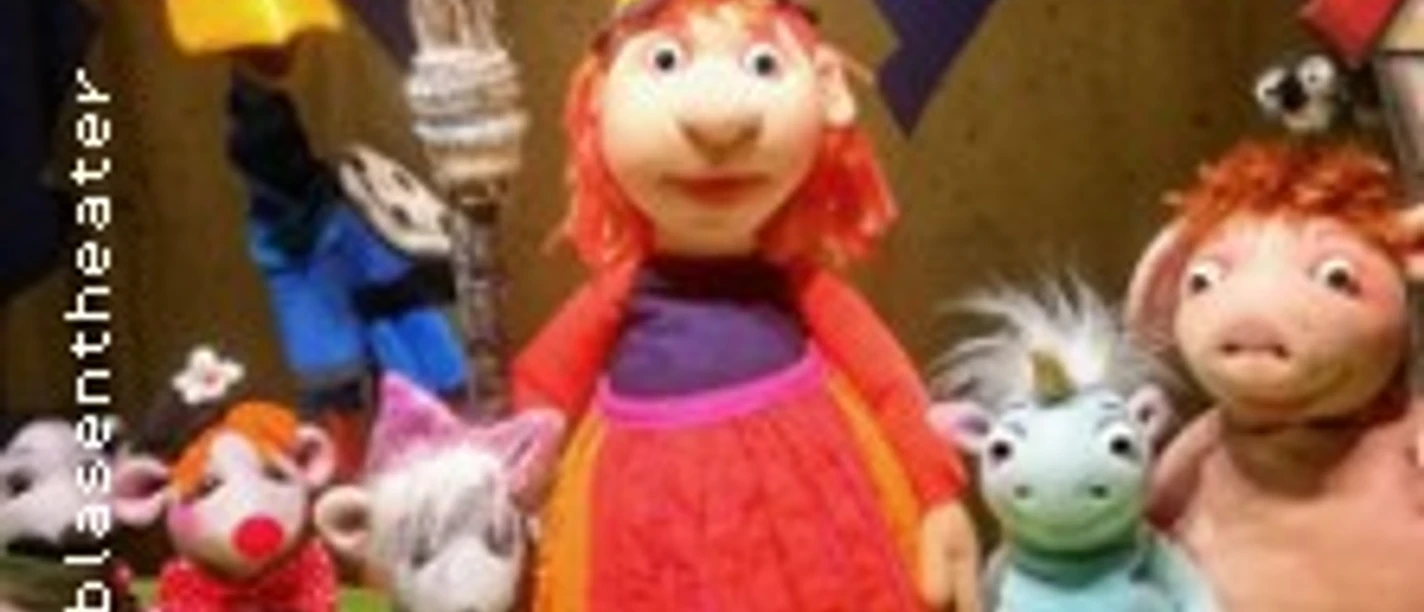 Bunte Handpuppen rund um eine kleine Hexenfigur stehen vor einer Kulisse mit Waldmotiv.