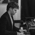 Ein junger Mann spielt konzentriert Klavier in einem schwarzweiß aufgenommenen Raum.