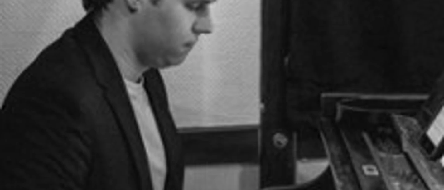 Ein junger Mann spielt konzentriert Klavier in einem schwarzweiß aufgenommenen Raum.
