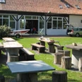 DLRG-Jugendbildungsstaette-Schirrhof_HD_16zu9.jpg DLRG-Jugendbildungsstätte mit Wiese, Steintischen, Holzhockern und einem Boot auf dem Hof.
