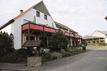 Außenansicht Ferienhof mit weißer Fassade, roten Balkonen und Innenhof in ländlicher Lage.