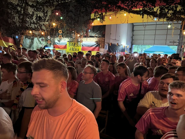 Wm Studio Viele Menschen beim Public Viewing in einer Halle mit Deutschlandflaggen und Lichterketten