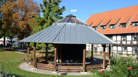 Gradierpavillon_Salzgitter_HD_16zu9.JPG Runder Holz-Gradierpavillon mit Metalldach in einer Grünanlage vor einem Fachwerkhaus.