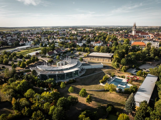 La vue aérienne montre la piscine Platsch avec son village de saunas à Oschatz ainsi que le panorama de la ville avec les clochers marquants de l'église St.Egidien en arrière-plan.