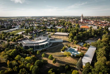 Letecký pohled ukazuje rekreační bazén Platsch se saunovou vesnicí v Oschatzu a panorama města s výraznými kostelními věžemi kostela svatého Egídia v pozadí.