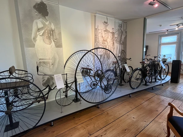 Historische Fahrräder, darunter ein Hochrad, ausgestellt im Museum vor großformatigen Wandbildern.