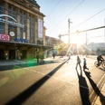Promenaden Hauptbahnhof Leipzig - Shopping in Leipzig Die Sonne steigt zwischen dem Promenaden Hauptbahnhof Leipzig und dem Wintergartenhochhaus auf, während Passanten den Willy-Brandt-Platz überqueren.