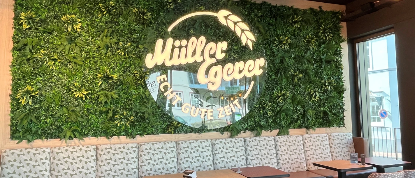 Interior of a café with a green wall logo by Müller Egerer above a modern seating area.