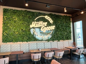 Müller Egerer Innenraum eines Cafés mit begrüntem Wandlogo von Müller Egerer über einer modernen Sitzgruppe.