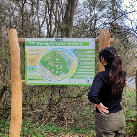 Trimmpfad - große Infotafel.jpg Eine Frau betrachtet die große Infotafel am Trimmpfad Klieversberg im Wald.