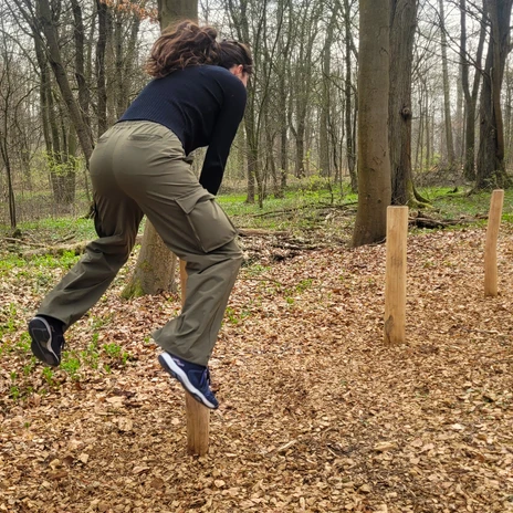 Trimmpfad - Bocksprung.jpg Frau beim Bocksprung über einen Holzpfahl auf einem Trimmpfad im Wald.
