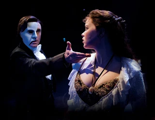 The Phantom of the Opera Masked man holds out his hand to a young woman in the dark stage light