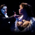 The Phantom of the Opera Masked man holds out his hand to a young woman in the dark stage light