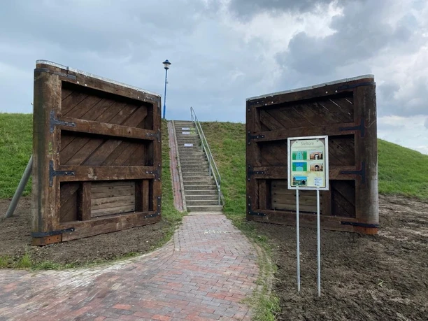 Alte Sieltore in Greetsiel Links und rechts stehen zwei alte braune Holz-Sieltore vor dem Deich. Davor ein Schaukasten mit Infos zu den Sieltoren.