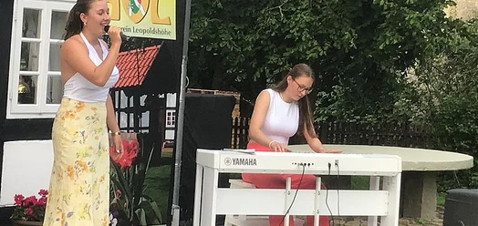 Sängerin mit Mikrofon und Pianistin am Keyboard beim Open-Air-Konzert auf dem Heimathof