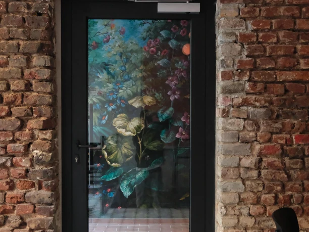 Glastür in Backsteinwand mit floral bemaltem Glas und gemustertem Fliesenboden