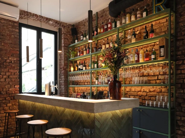 Kleine Bar mit Backsteinwänden, beleuchtetem Tresen und hohen Hockern