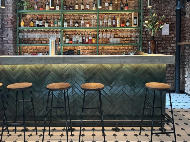 Bar Moderne Bar mit Backsteinwand, grüner Theke, hohen Hockern und gefüllten Regalen.