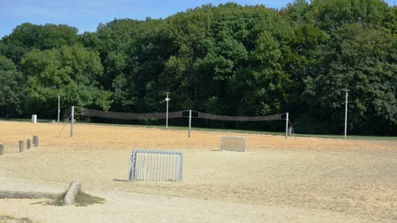 Weites Sandfeld am Salzgittersee mit Beachvolleyballnetz und zwei Toren vor grünen Bäumen.