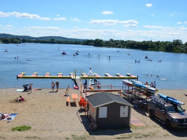 Sandstrand am Salzgittersee mit Bootsverleih, Steg und aktiven Wassersportlern auf dem See.
