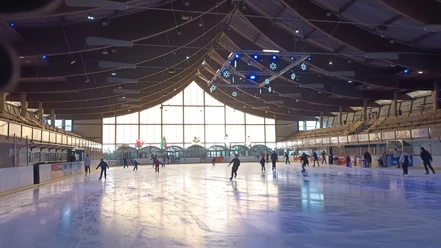 Zahlreiche Menschen laufen in der hellen Eissporthalle mit Holzdecke Schlittschuh.