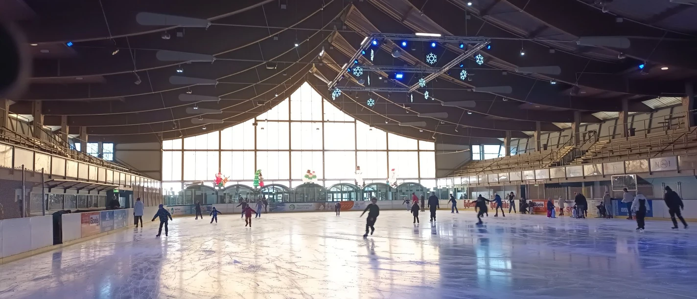 Eislaufen_Salzgittersee (4)_HD_16zu9.jpg Zahlreiche Menschen laufen in der hellen Eissporthalle mit Holzdecke Schlittschuh.