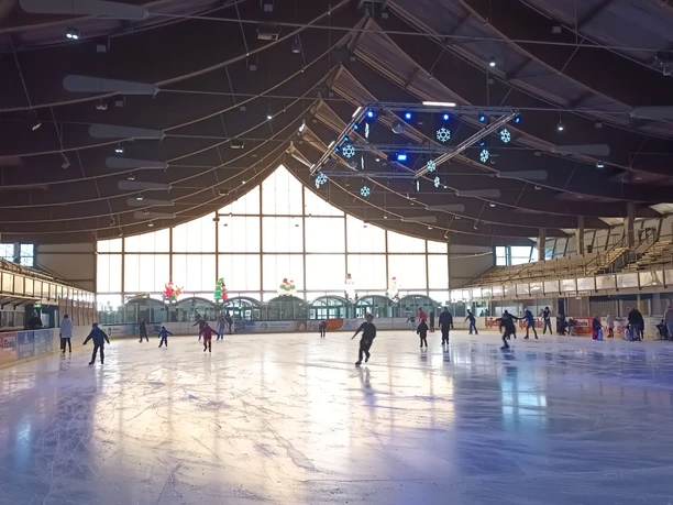 Eislaufen_Salzgittersee (4)_HD_16zu9.jpg Zahlreiche Menschen laufen in der hellen Eissporthalle mit Holzdecke Schlittschuh.