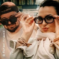 Marie-Claire und Rafael posieren mit Sonnenbrillen, eine Hand formt ein OK-Zeichen.