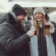 Epic Escape Two people in winter coats drink hot mulled wine outside and laugh together