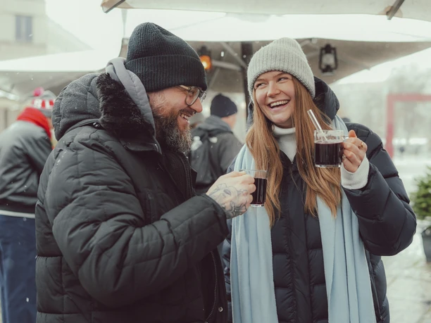 Epic Escape Zwei Personen im Wintermantel trinken draußen heißen Glühwein und lachen miteinander