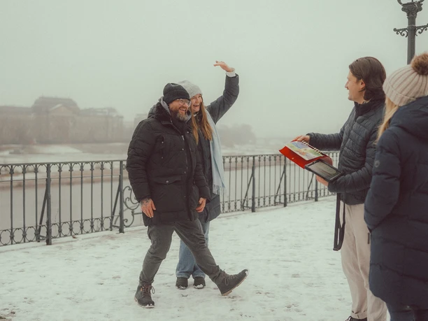 Epic Escape Gruppe auf verschneiter Uferpromenade, vertieft in ein Rätselbuch bei winterlichem Nebel
