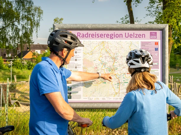 Radfahrer an Übersichtstafel der Radreiseregion Uelzen Zwei Radfahrer mit Helmen betrachten eine Übersichtskarte der Radreiseregion Uelzen im Freien