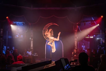 „Fly Me to the Moon – Sinatra meets Varieté“ Akrobatin posiert am beleuchteten Halbmond im Spiegelpalast vor Publikum.