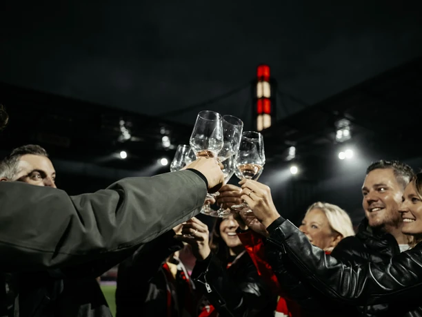 WeintastingTour Gruppe stößt nachts im Stadion mit leeren Weingläsern an.