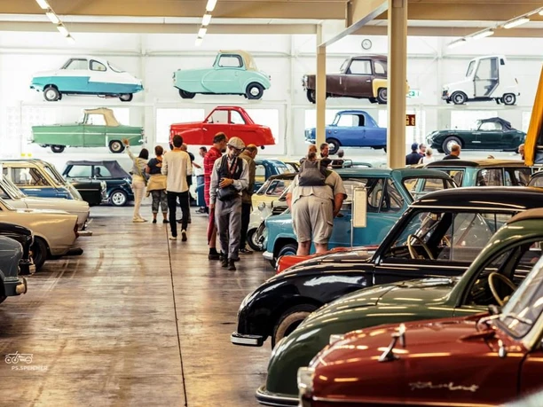 Sammlung KLEINWAGEN Besucher betrachten historische Kleinwagen in einer hellen, weitläufigen Ausstellungshalle.