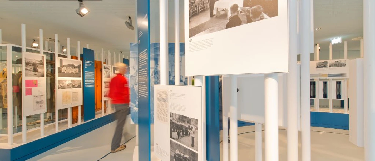 Ein heller Ausstellungsraum mit Infotafeln, die sowohl Text als auch Bilder zeigen.