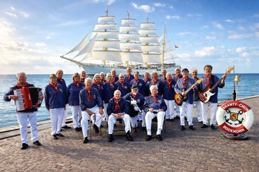 Shanty Chor Bockhorn Shanty Chor Bockhorn an Küste maritim gekleidet. Im Hintergrund ist ein Schiff zu sehen.