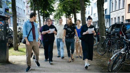 Stadtspaziergang1 Gruppe beim Stadtspaziergang auf einer von Bäumen gesäumten Straße in Köln