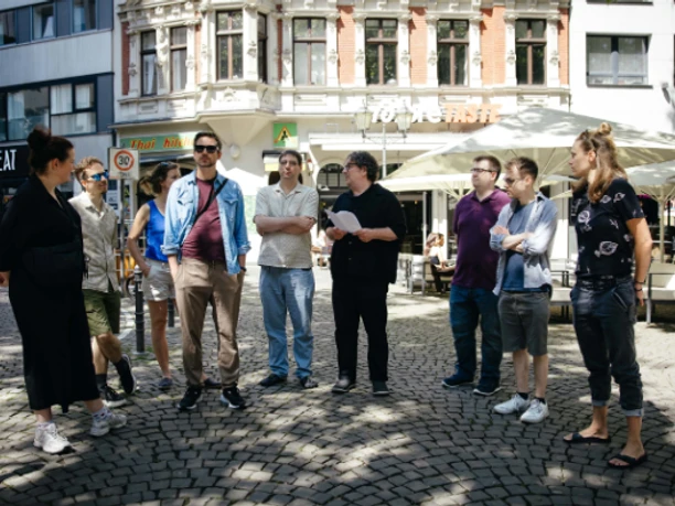 Stadtspaziergang4 Gruppe bei einem Stadtspaziergang auf einem Kölner Platz vor Cafés und Altbaufassade