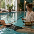 Wasser und Klang KI generiert.png Zwei Frauen im Thermenbad: Eine treibt entspannt, die andere spielt sanft eine Klangschale.