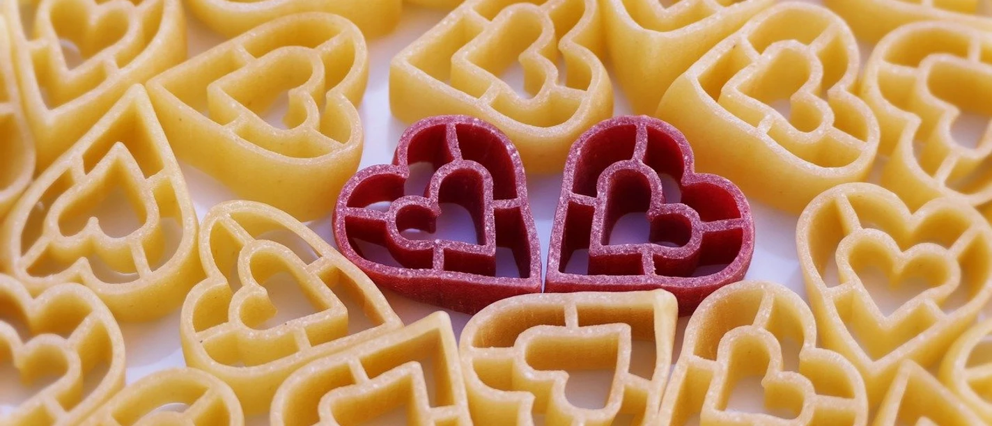 Beziehungen Zwei rote Herznudeln leuchten liebevoll zwischen vielen gelben Nudeln hervor.