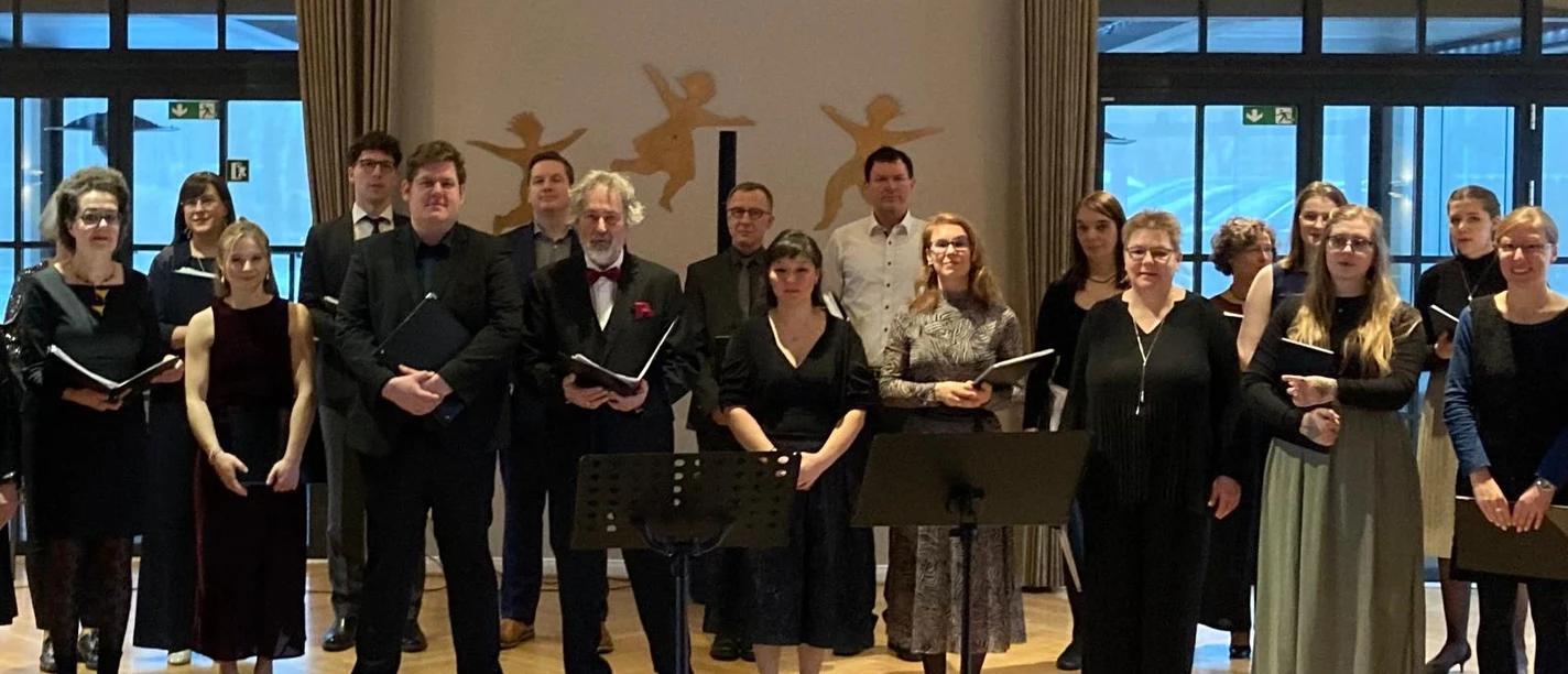Das Gesangensemble Ein gemischter Chor in dunkler Kleidung steht mit Notenmappen für ein Konzert bereit.