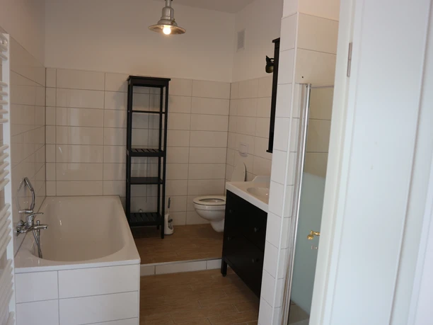 Helles Bad mit Badewanne, WC, Waschbecken, Regal und Dusche mit Glasabtrennung