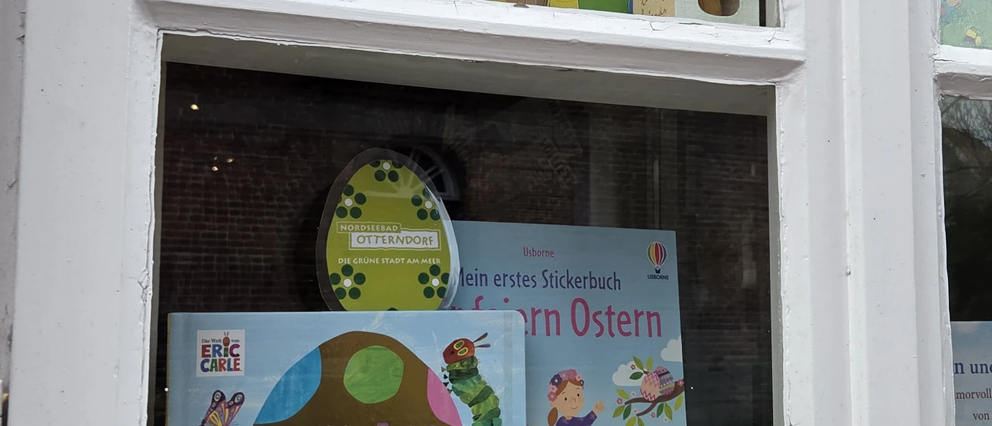 Osteraktion Bild Bunte Osterbücher und Holzhasen schmücken ein weißes Fenster zur Osteraktion in Otterndorf.