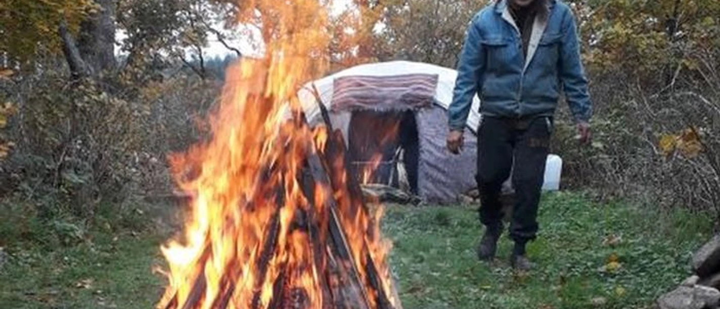 Schwitzhütte Wingst Loderndes Lagerfeuer vor einer Schwitzhütte im Wald. Ein Mann geht in der Natur daran vorbei.