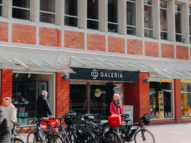 Galeria Lüneburg Kaufhaus Galeria in Lüneburg mit roter Backsteinfassade und großen Fenstern, davor Fahrräder und Passanten.