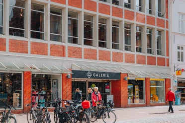 Galeria Lüneburg Kaufhaus Galeria Lüneburg in einem roten Backsteingebäude, davor Passanten und Fahrräder.